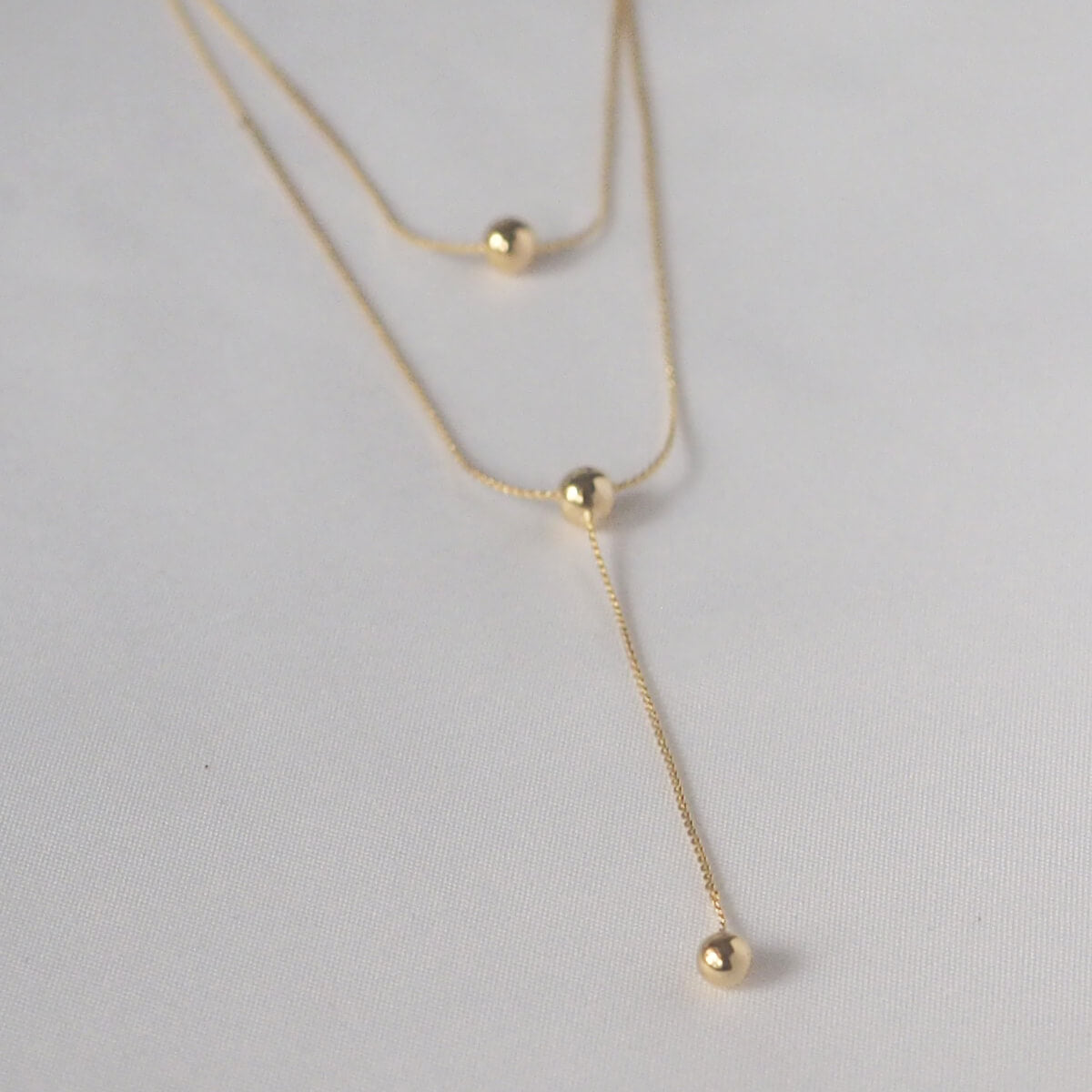 Chic double chain necklace with two gold balls, adjustable lengths for a stylish and minimalist look.