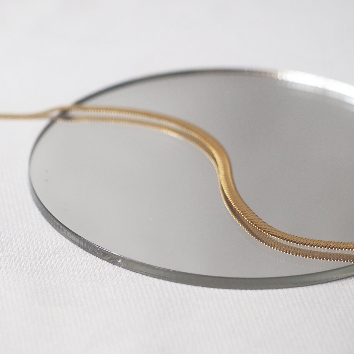 A shimmering gold chain rests elegantly on a mirror, reflecting its sleek design and luxurious appeal.