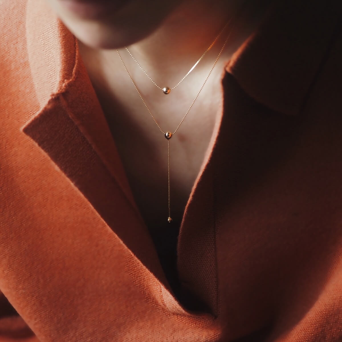 A woman models a black shirt and a glamorous gold double chain necklace with a ball pendant, perfect for any occasion.