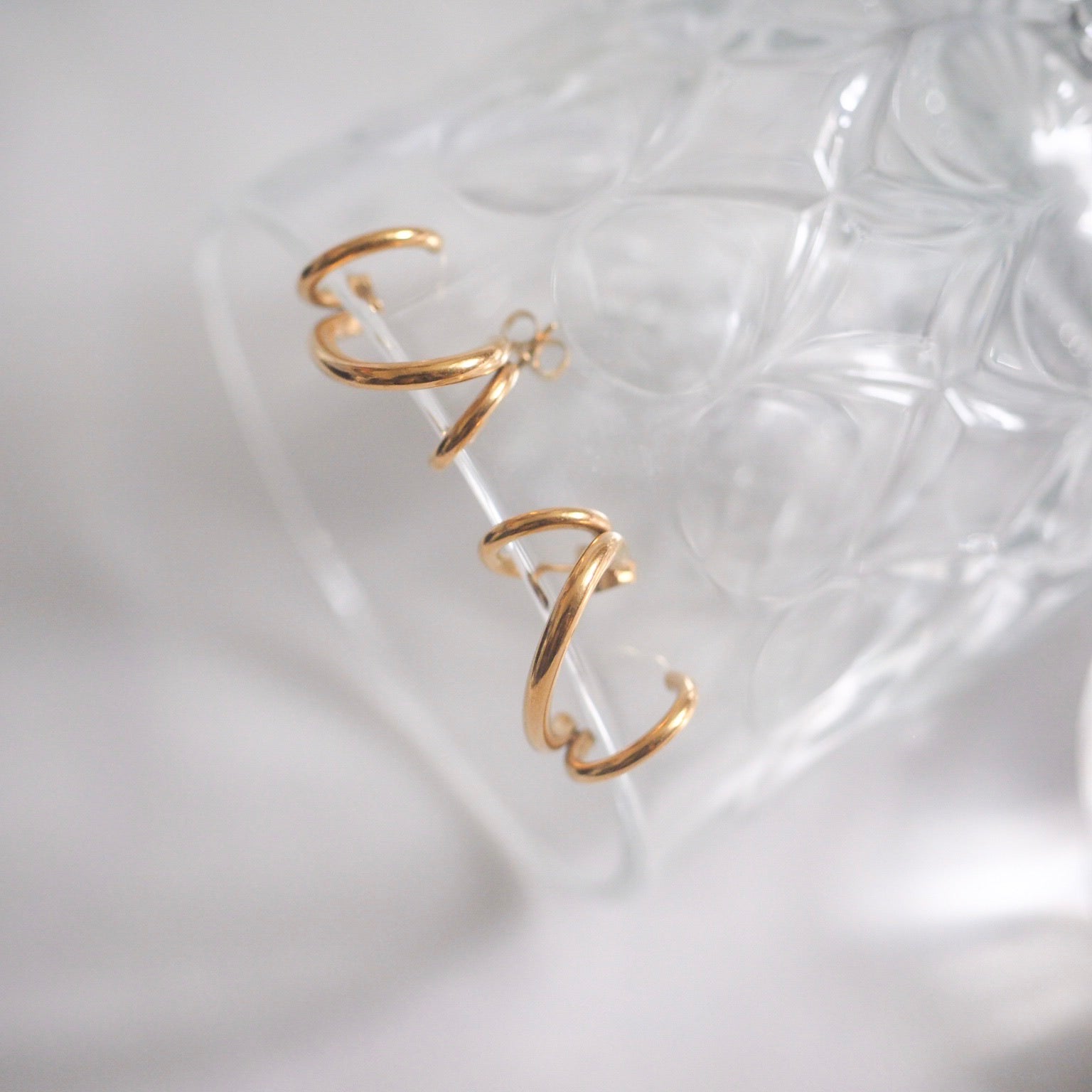 Gold hoop earrings with a helix spiral design elegantly displayed on a glass table, crafted from 18K gold plated stainless steel.