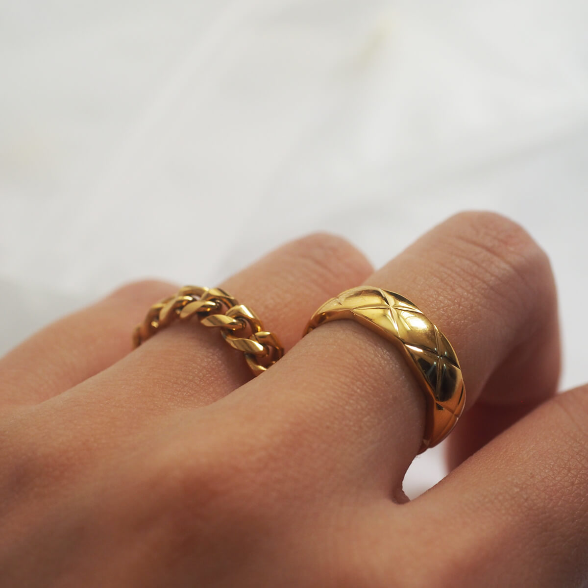 A hand displaying two polished gold rings, beautifully engraved with an "X" pattern, perfect for making a statement.
