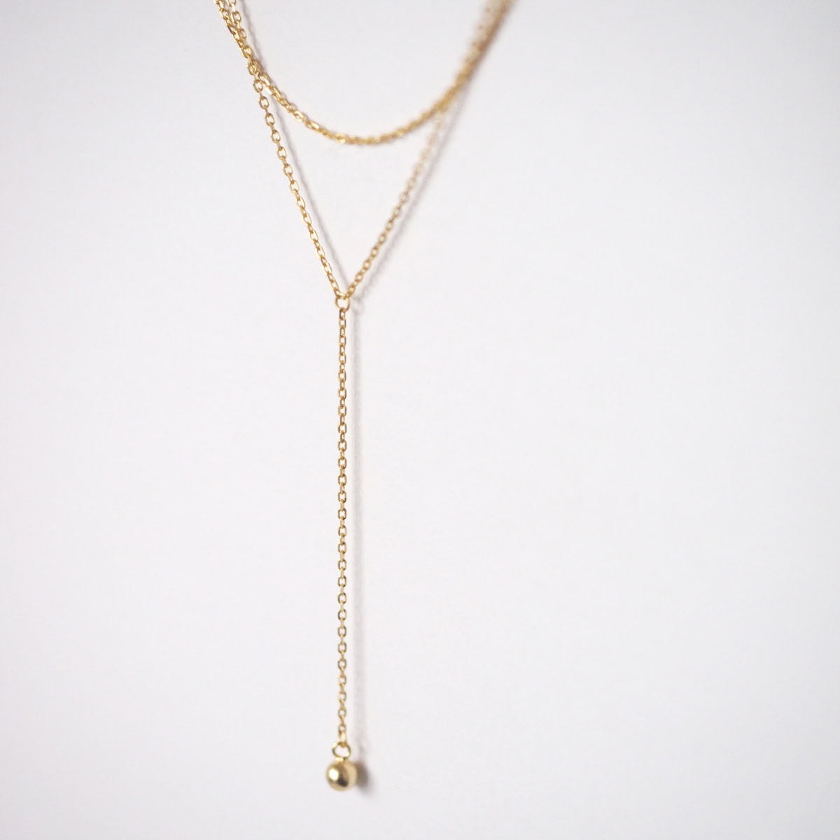 Close-up view of the Mone Ball Drop Necklace showing dual gold vermeil chains and a dangling bead.