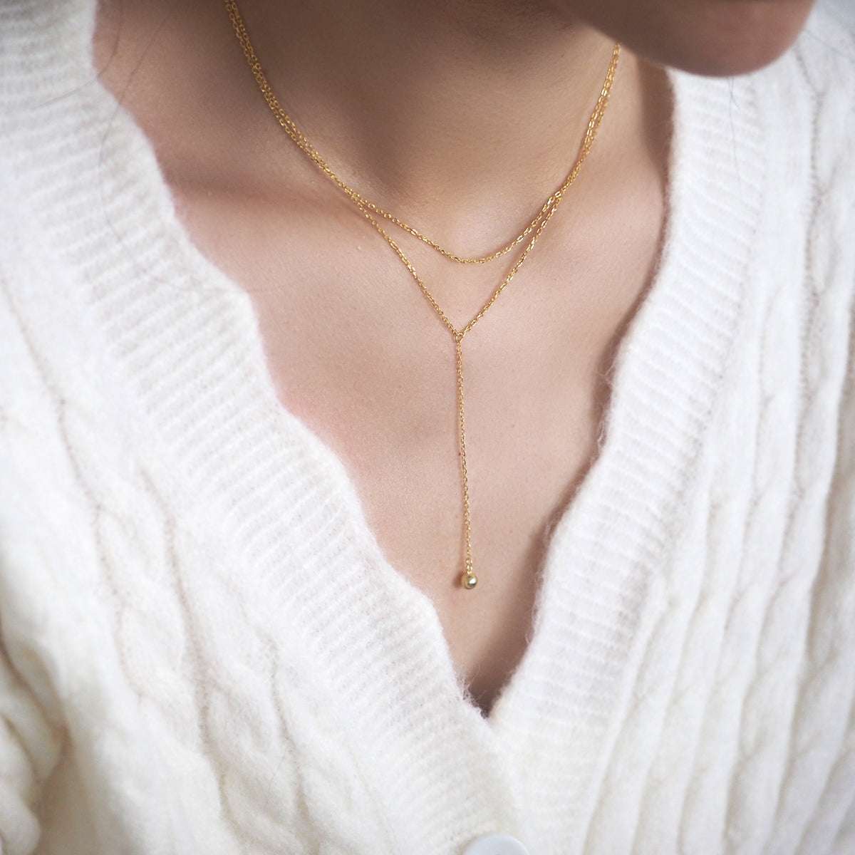 Woman wearing the Mone Ball Drop Necklace layered over a white knit sweater.