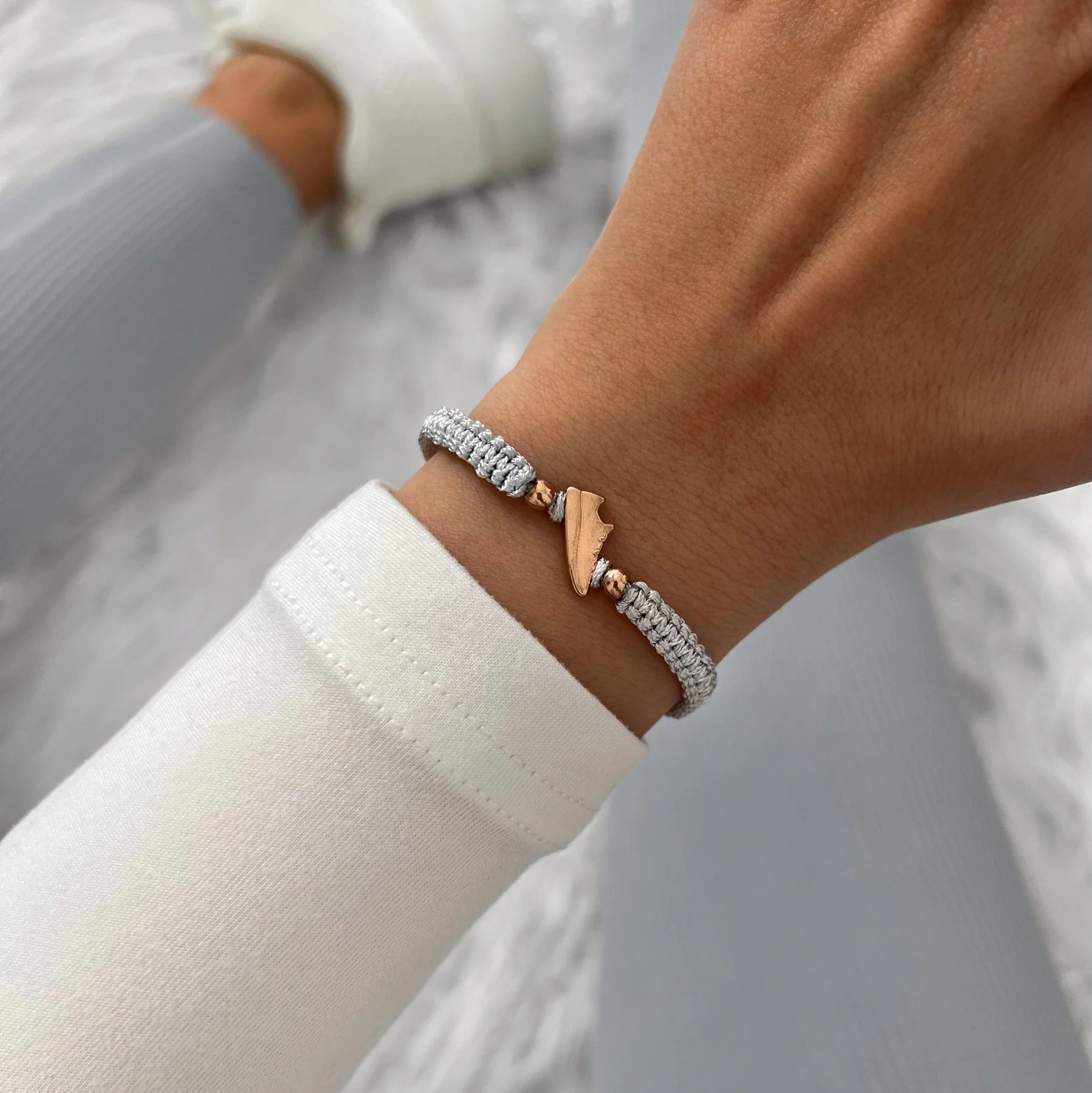 Rose Runner Grey Braided Bracelet on a wrist, paired with a white sweater and matching grey activewear, showcasing a sporty-chic look.