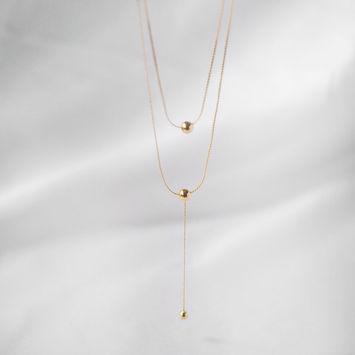Stunning double-layer gold necklace with long strands of beads and a stylish ball pendant, ideal for any outfit.