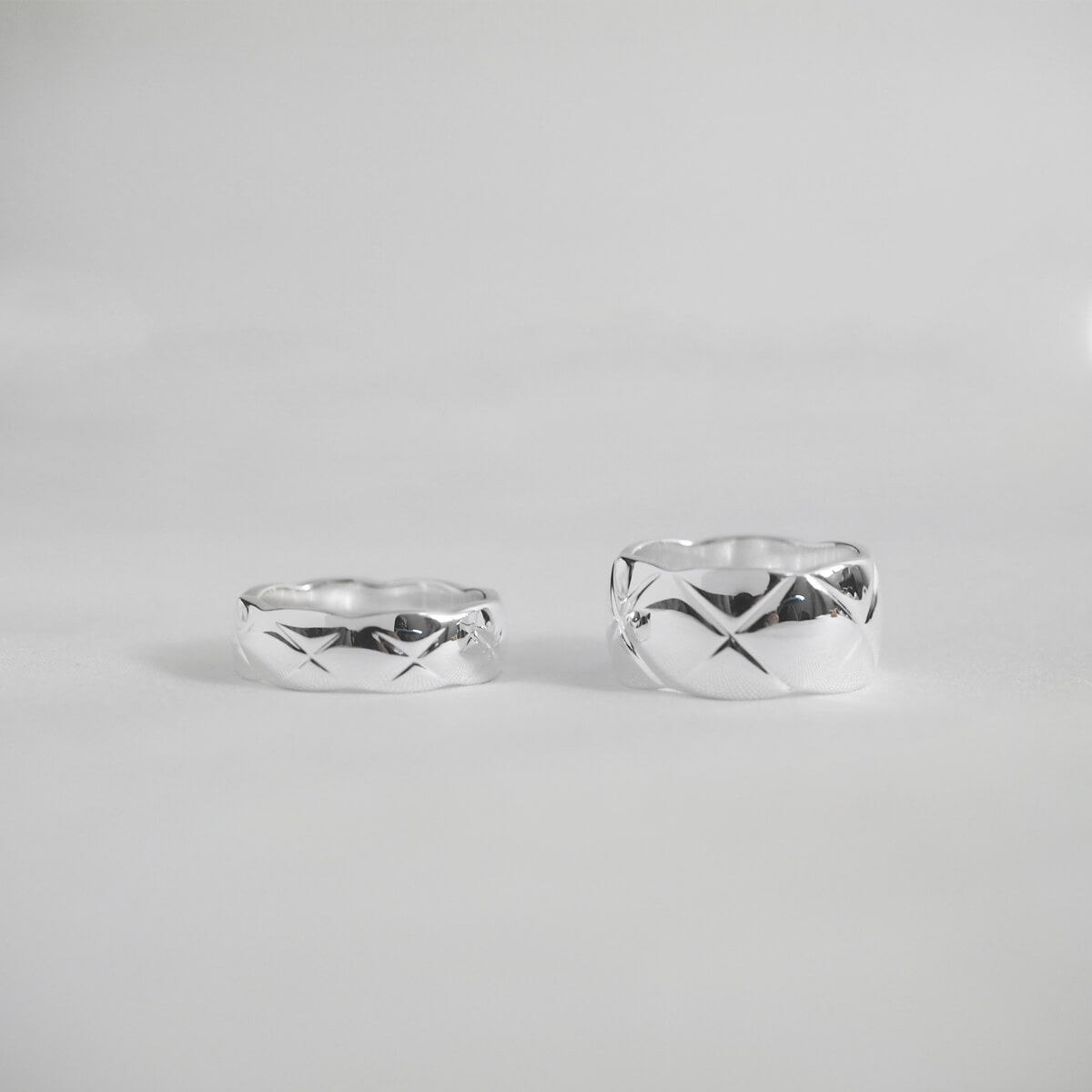 Two stylish silver rings with a diamond pattern and X motif engravings, perfect for adding a touch of elegance to any outfit.