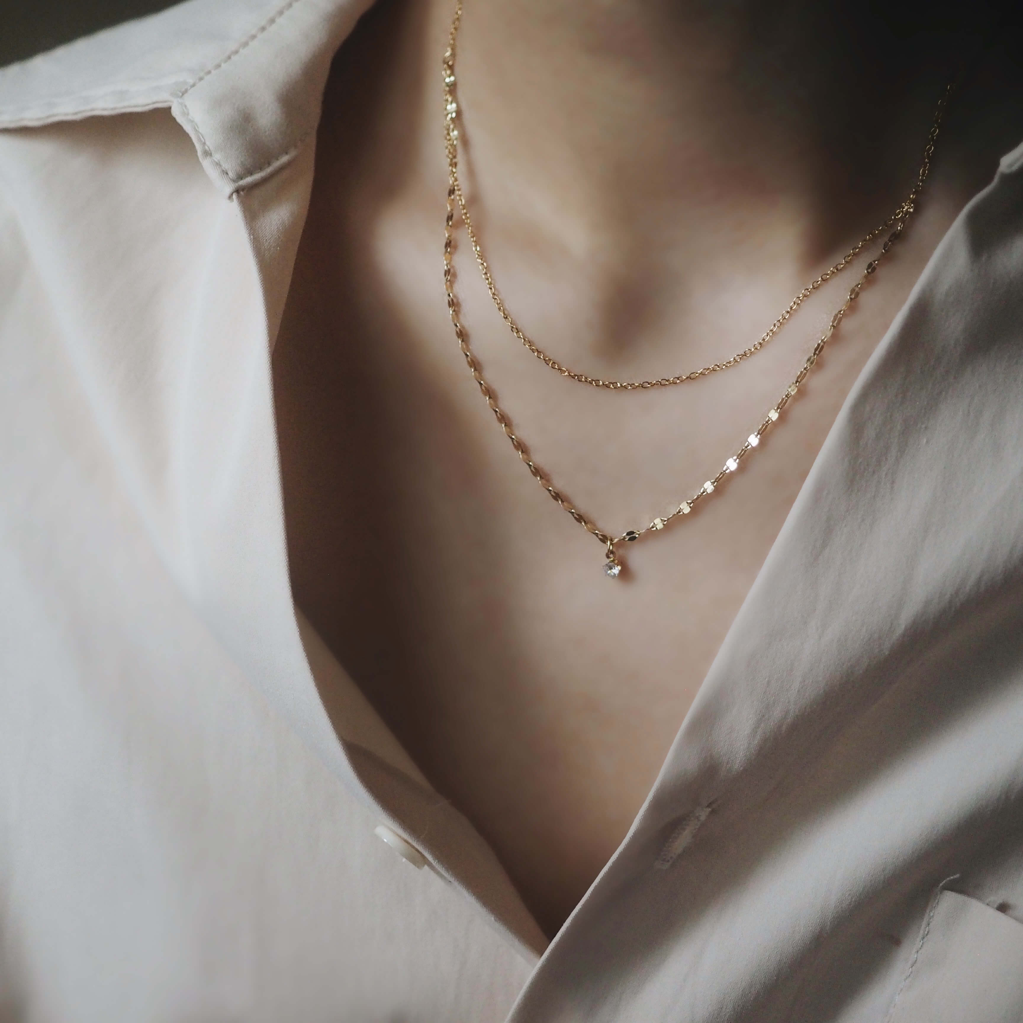 A woman dressed in a white shirt, complemented by a shimmering gold necklace, showcasing a refined appearance.