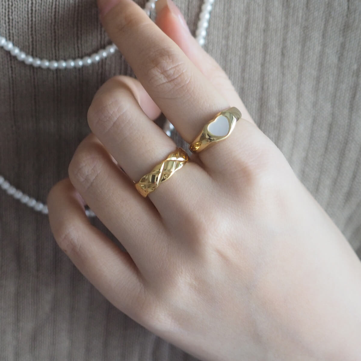 A woman elegantly displays a gold ring with pearls, highlighted by a unique "X" motif engraving for a striking look.