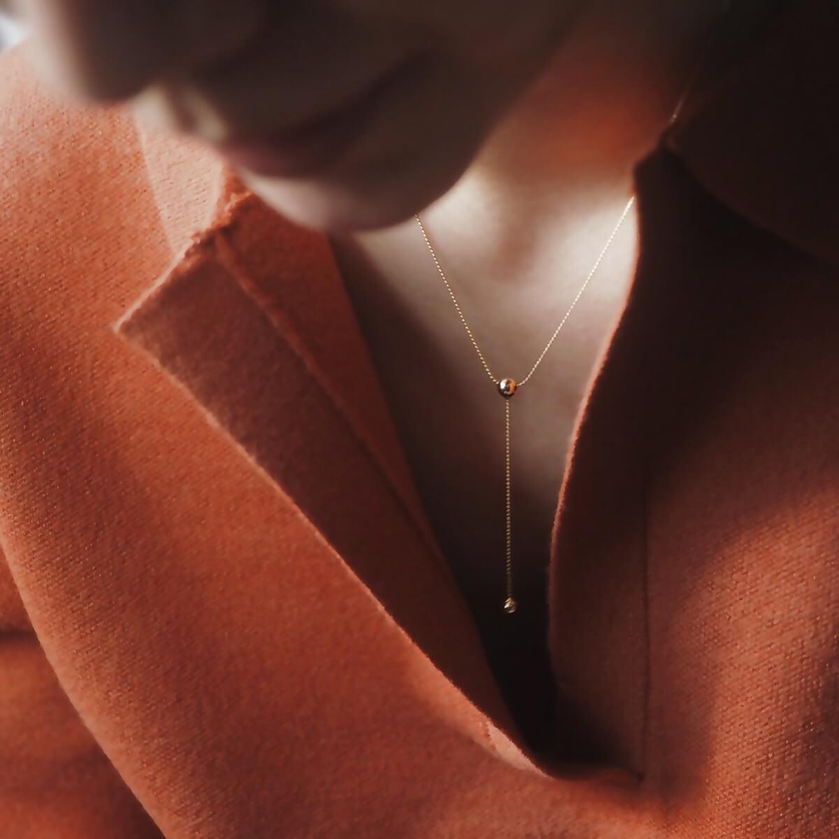 A woman wearing a red shirt models a chic gold double chain necklace with a ball pendant, enhancing her stylish appearance.