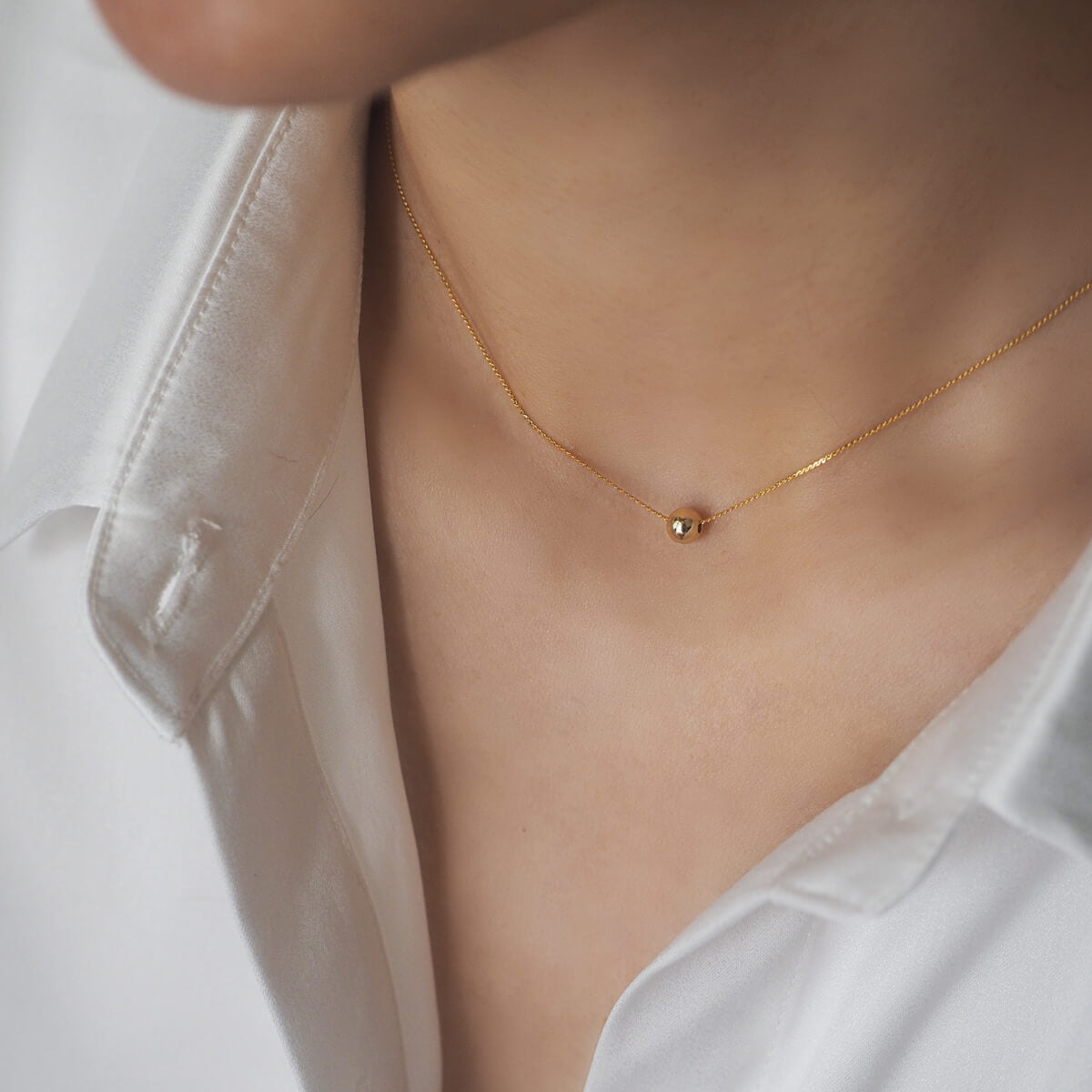 A woman models a chic gold necklace with a small ball pendant, perfect for a glamorous and minimalist style.
