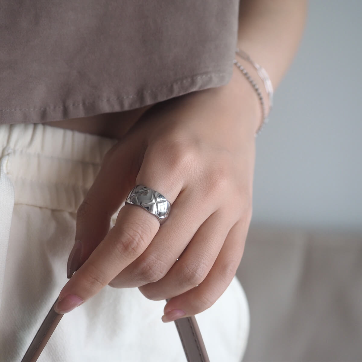 A close-up of a woman's hand adorned with a striking silver ring featuring deep "X" engravings, perfect for any occasion.