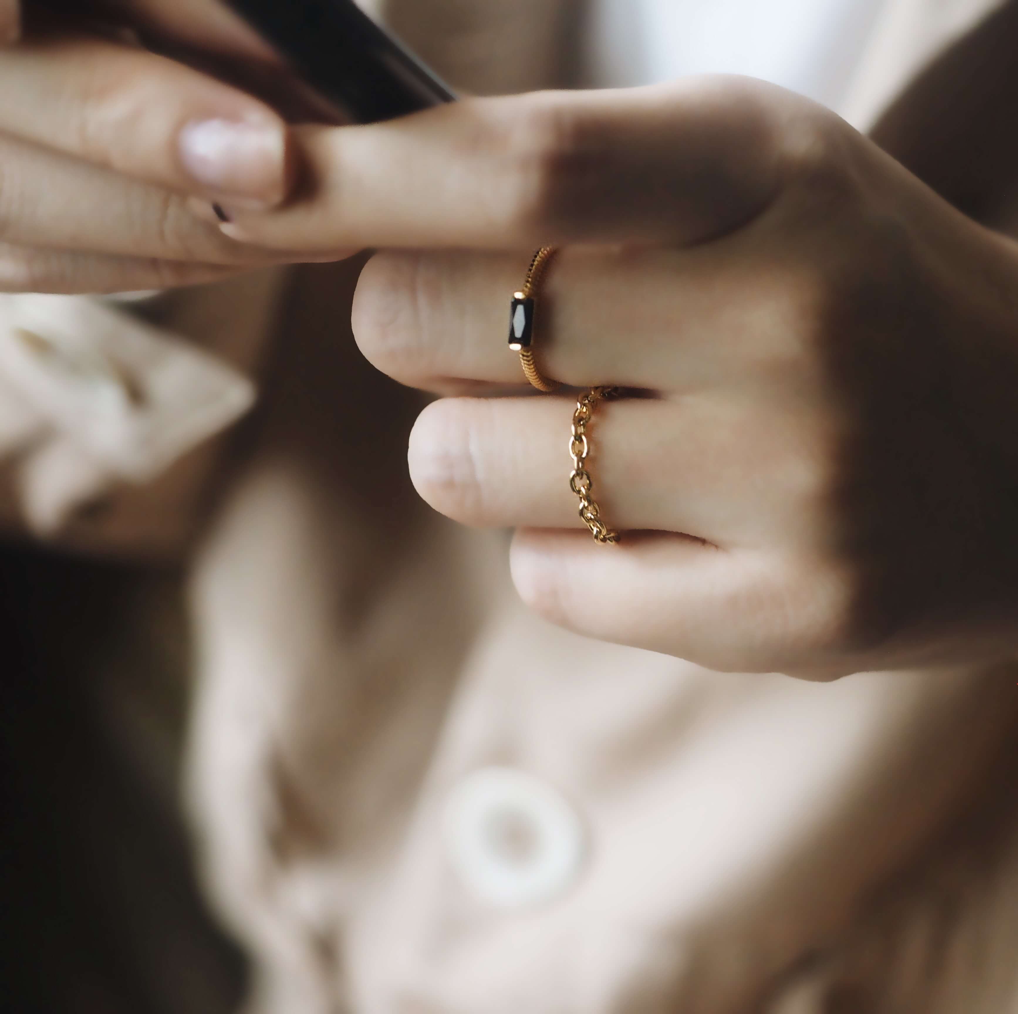 A woman displays a gold ring on her finger while holding a cell phone, blending elegance with technology.