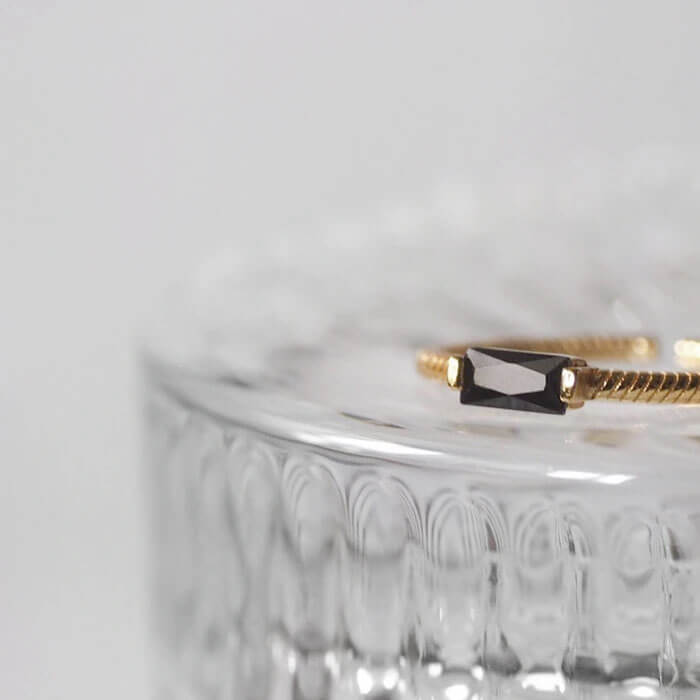 Timeless gold ring adorned with a mesmerizing black cubic zirconia stone, displayed on a transparent glass table.