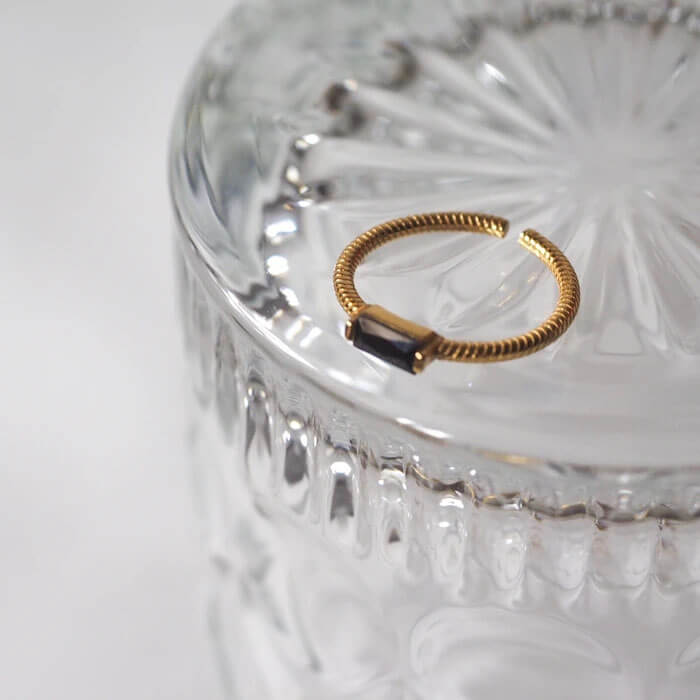 A shimmering gold ring elegantly rests on a sleek glass table, reflecting light beautifully.