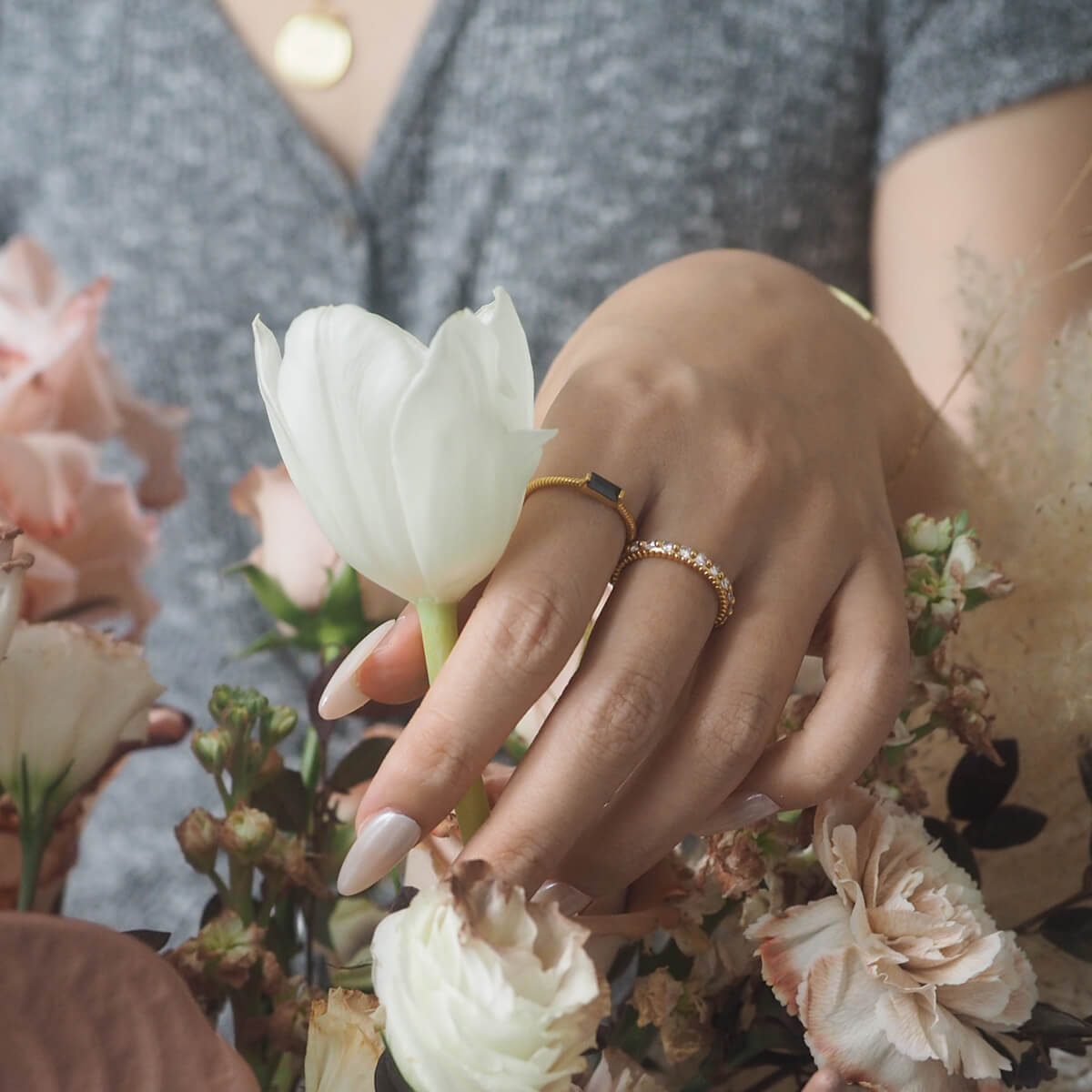 A woman with a joyful expression holds a bouquet of flowers, highlighting a beautiful ring on her finger.