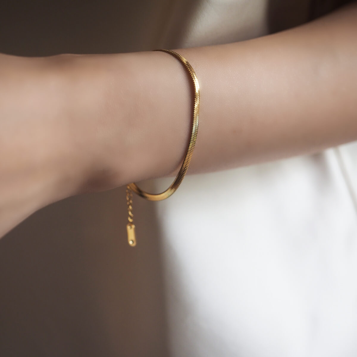 A stylish woman displays a gold bracelet on her wrist, emphasizing its classy design and adjustable length for a perfect fit.