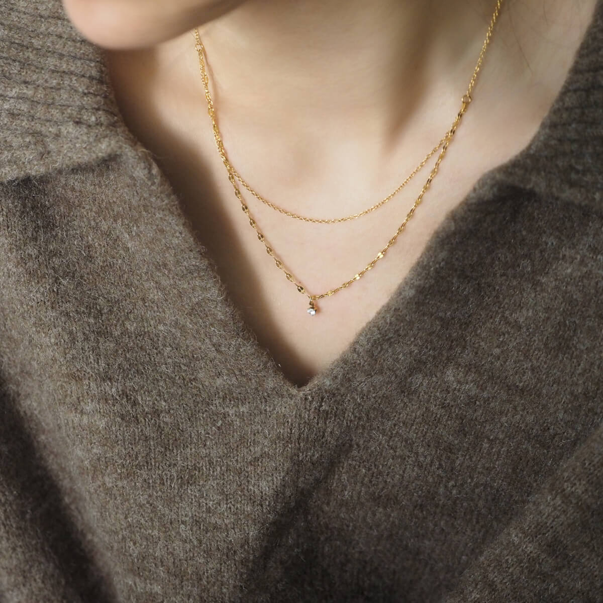 A woman in a stylish sweater, complemented by a shimmering gold necklace, radiating sophistication and comfort.