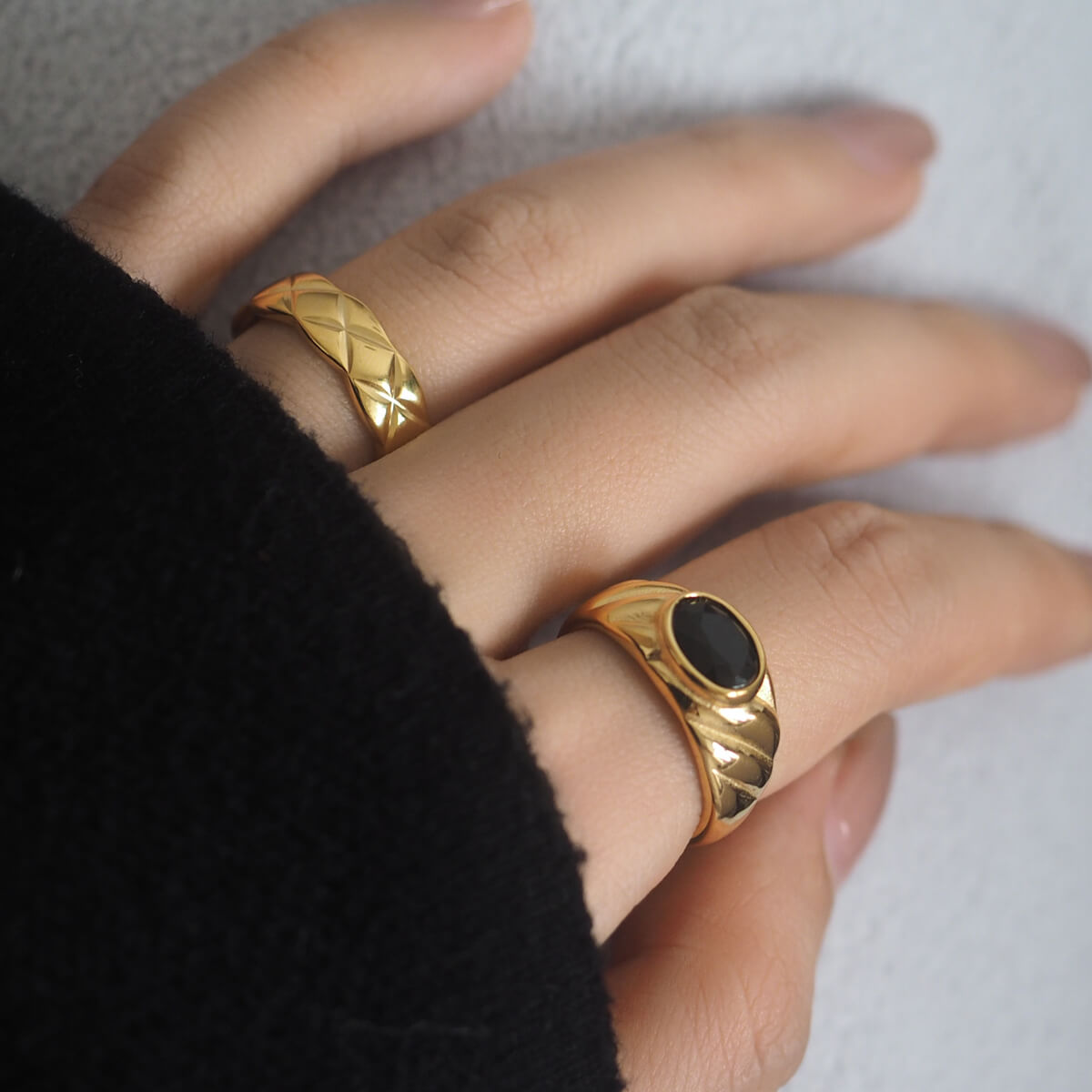 Two elegant rings featuring black stones, set in polished gold or silver with an intricate "X" motif engraving.