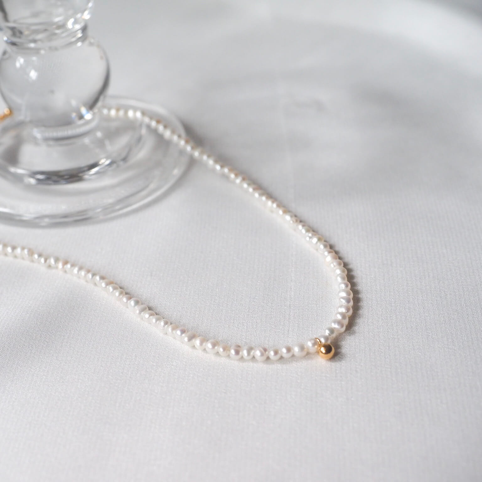 Elegant white pearl necklace with a gold clasp and a tiny golden bean charm, perfect for a minimalistic style.