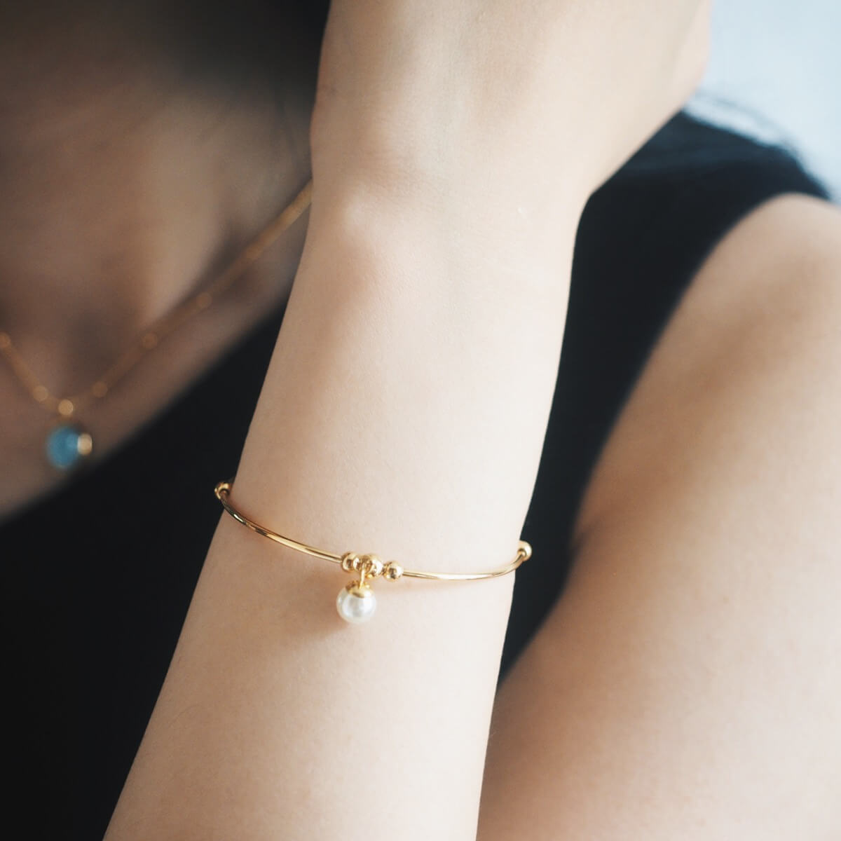 A woman elegantly displays a gold bracelet with a pearl, emphasizing her chic fashion sense and refined taste.