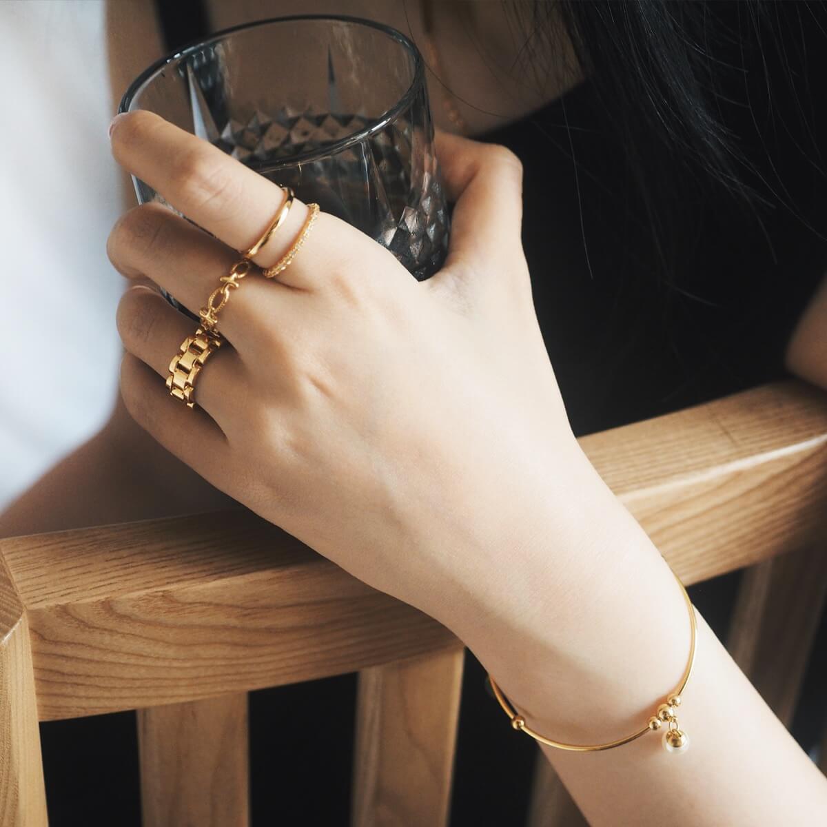 A woman elegantly holds a glass while showcasing a gold ring on her finger, exuding sophistication and style.