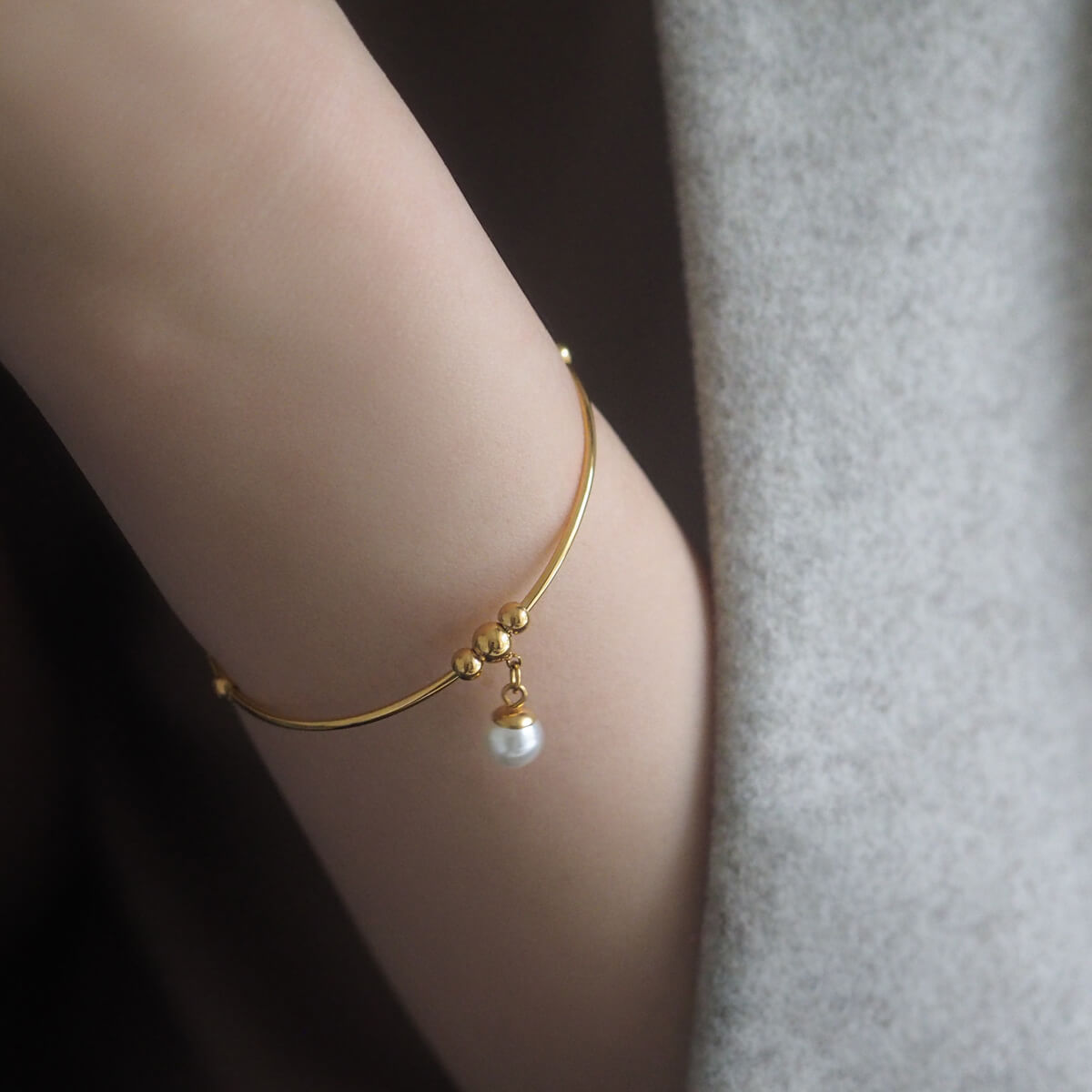 A close-up of a woman's wrist featuring a stunning gold bracelet, beautifully complemented by a single, radiant pearl.