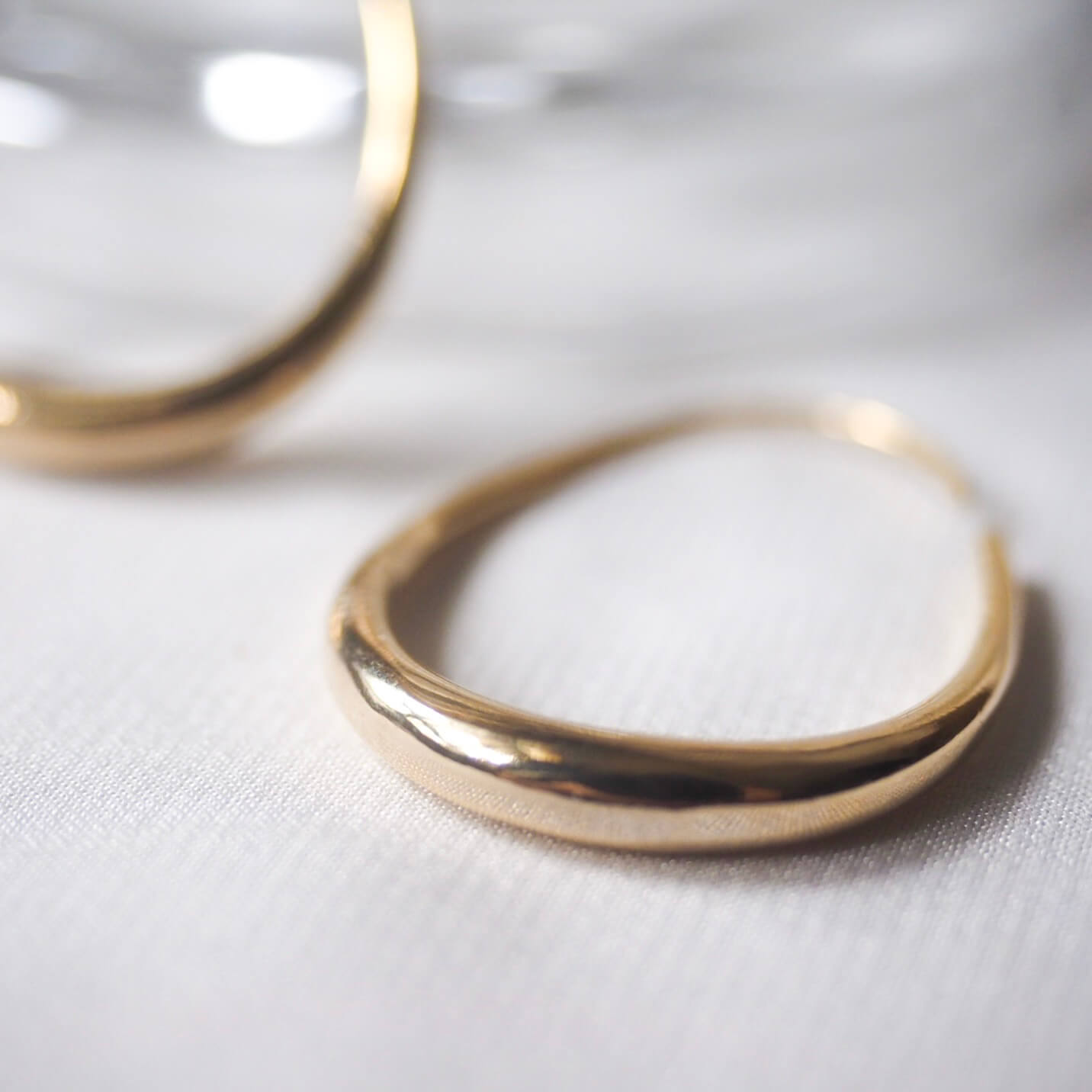 Shiny gold hoop earrings displayed on a pristine white cloth, highlighting their stylish and timeless appeal.