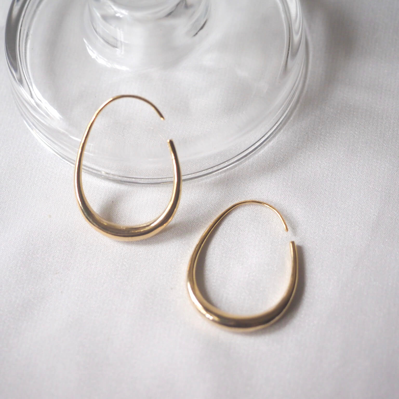 A pair of elegant gold hoop earrings resting on a soft white cloth, showcasing their shine and intricate design.