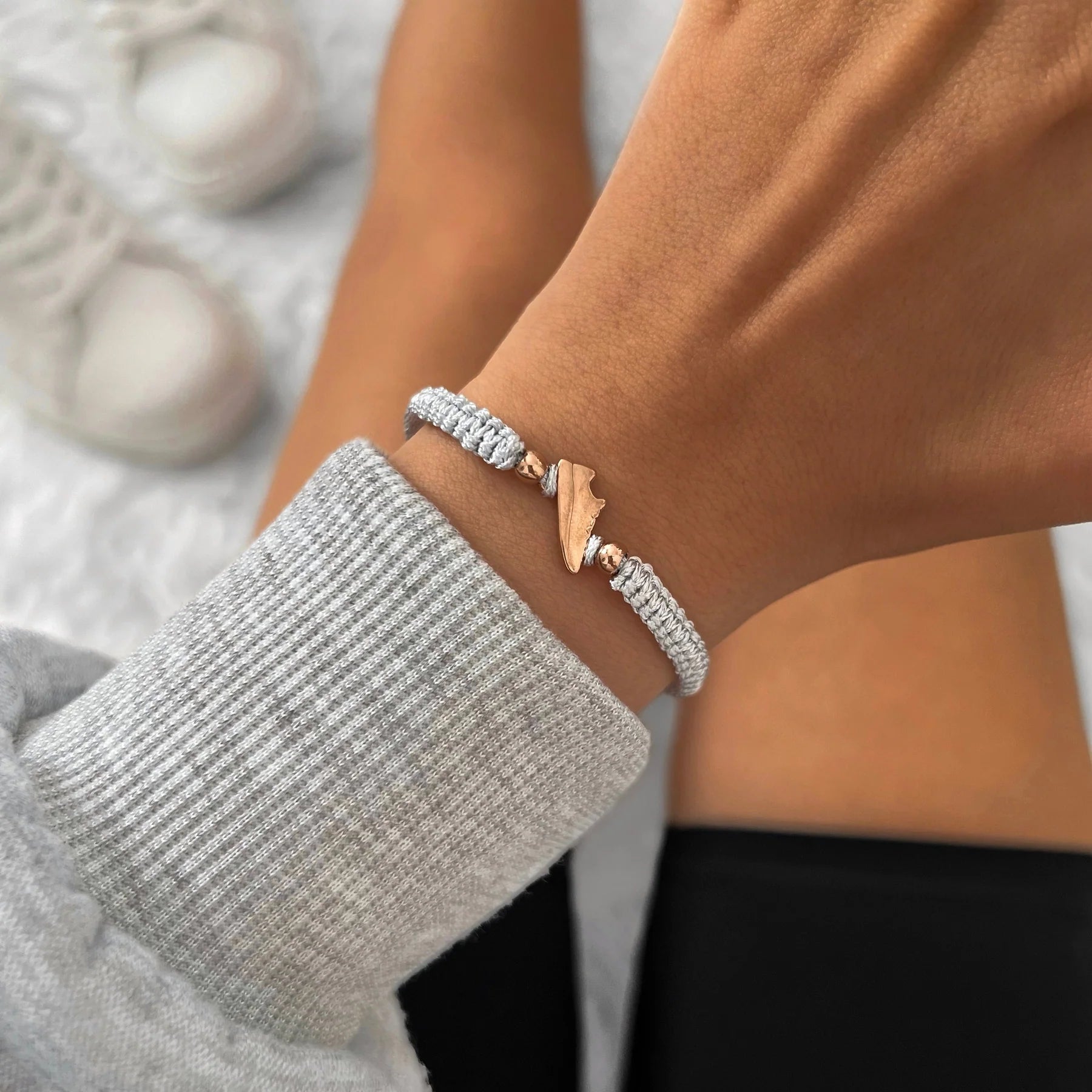 Rose Runner Grey Braided Bracelet worn on a wrist, styled with a grey ribbed sweatshirt and white sneakers in the background.
