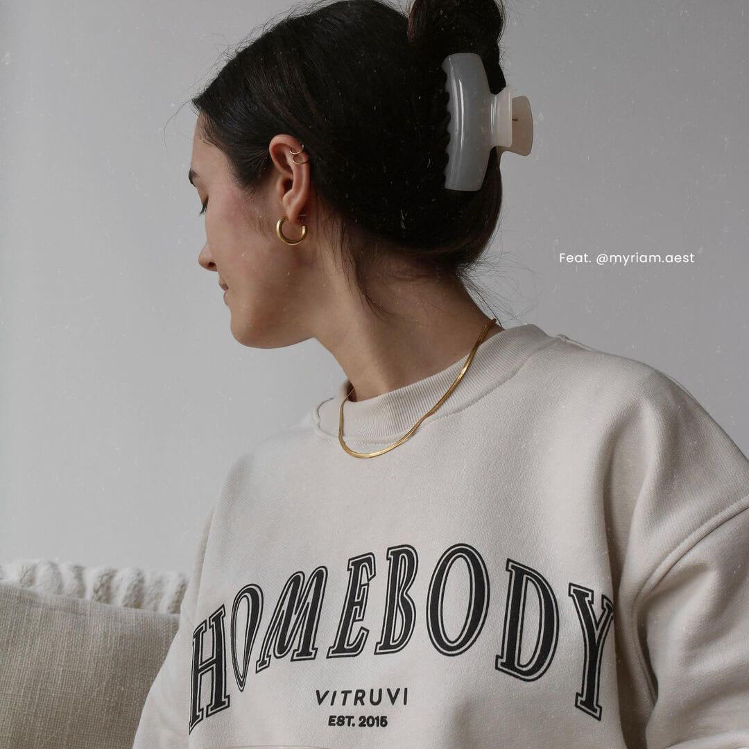 A stylish woman dons a "homebody" sweatshirt, exuding comfort and charm, featuring @myriam.aest.