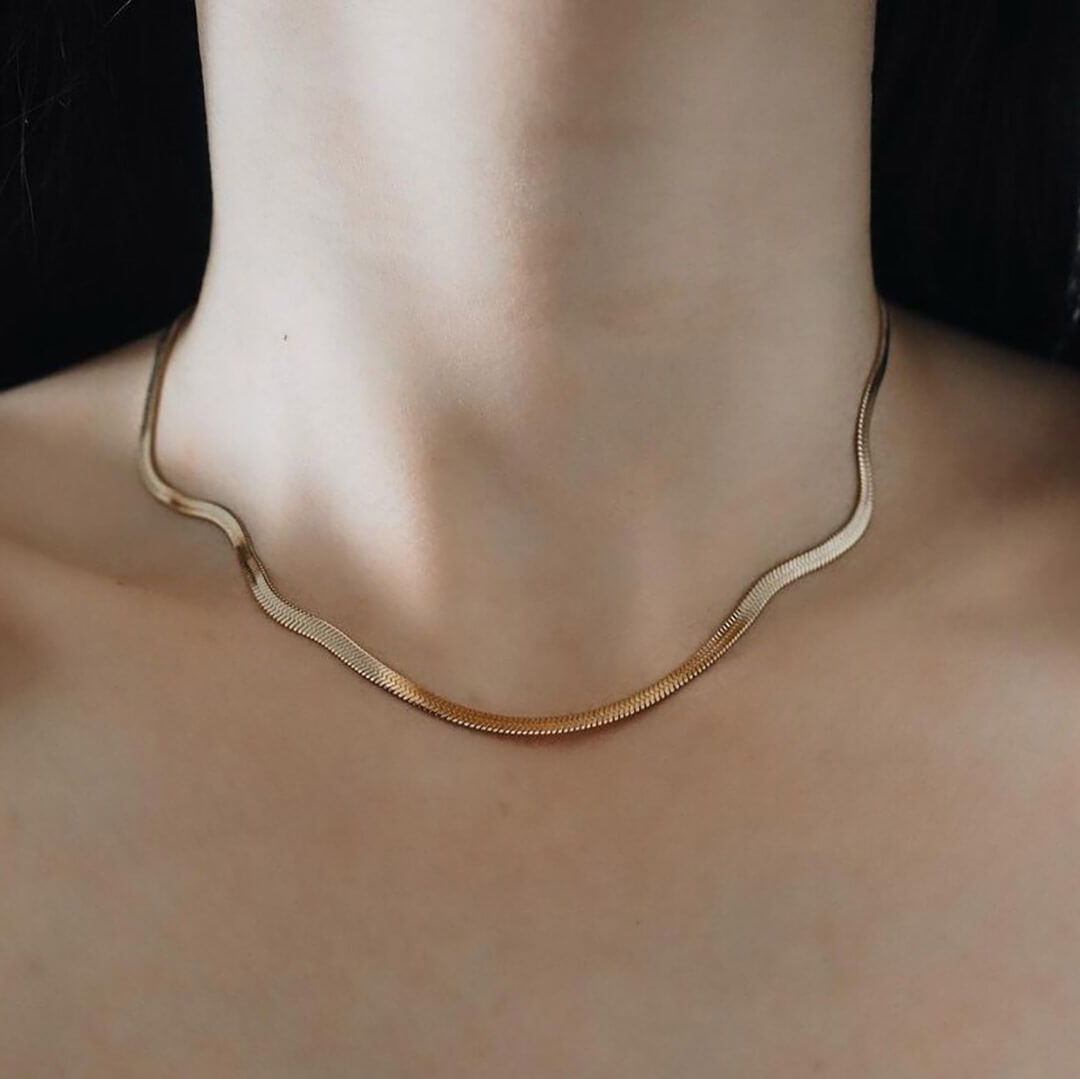 A woman elegantly wears a gold necklace featuring a graceful curved shape, enhancing her style and beauty.