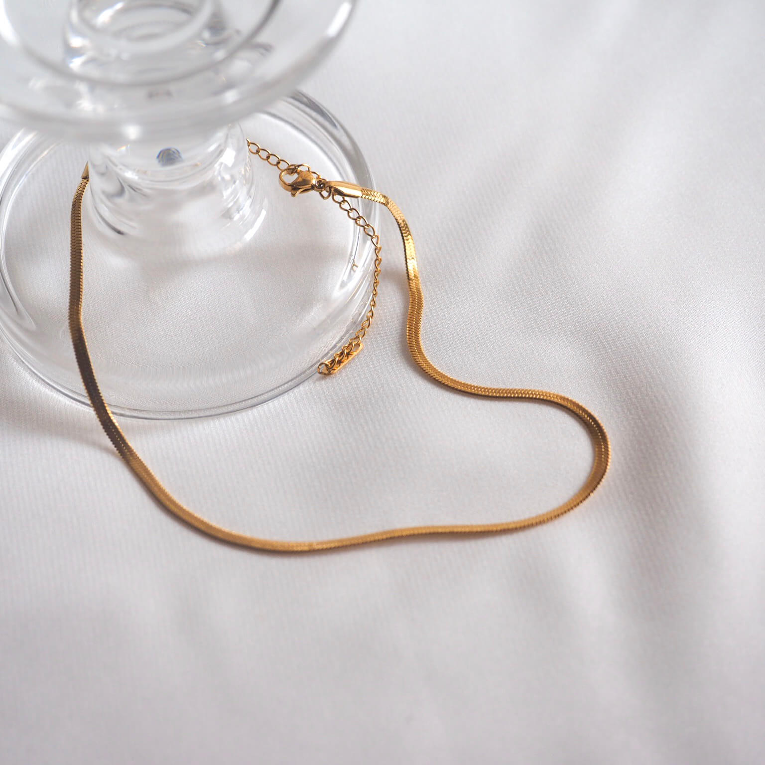 A shimmering gold chain necklace elegantly draped over a soft white cloth, showcasing its luxurious shine and texture.