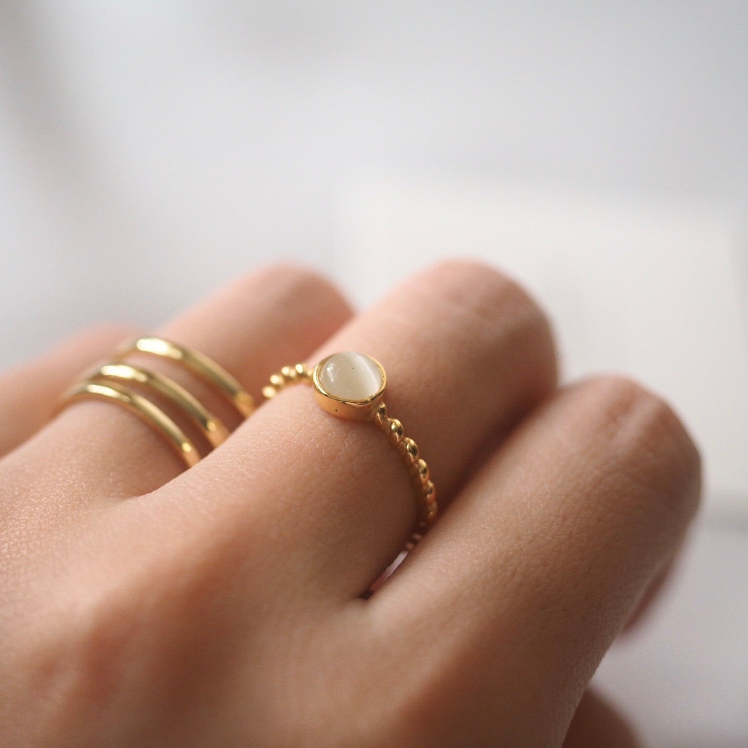 A woman's hand displays a gold ring with a white opal stone, highlighting its classic and stunning design.