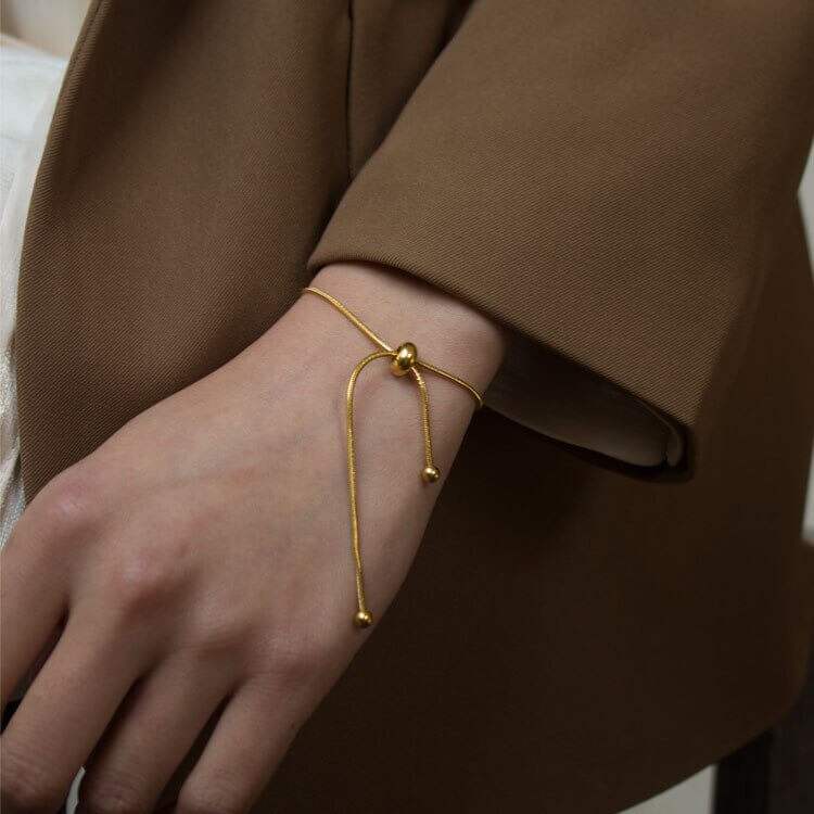 A woman’s wrist is elegantly decorated with a shimmering gold bracelet, emphasizing her fashionable accessory choice.