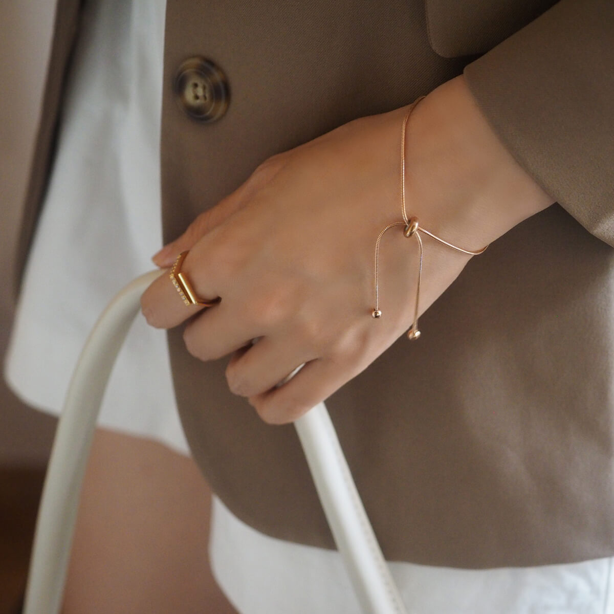 A woman in a stylish jacket holds a white bag, exuding confidence and modern fashion.