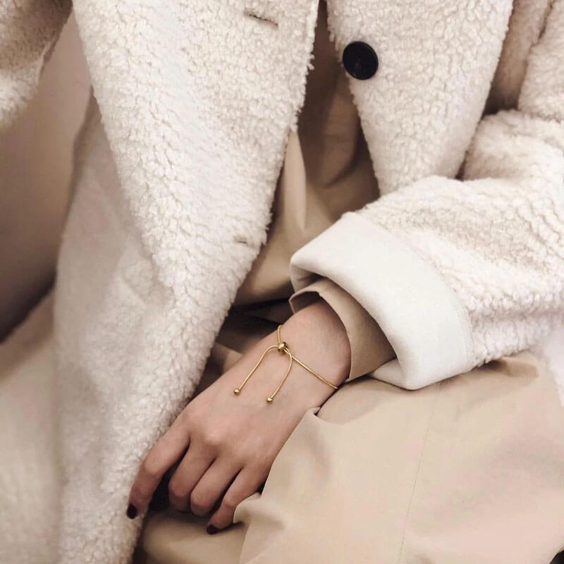 A fashionable woman dons a crisp white coat, complemented by a striking gold bracelet that adds a touch of glamour.