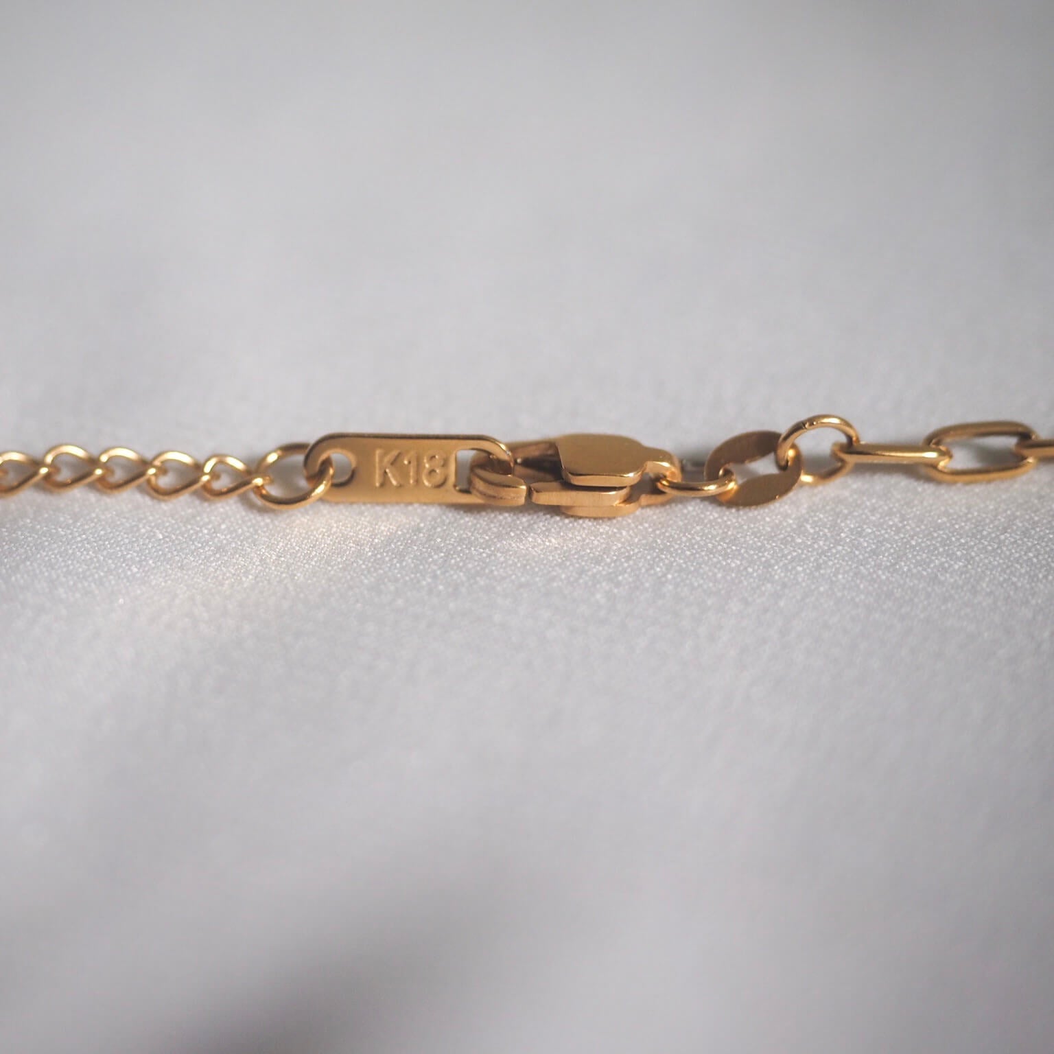 A close-up of a gold chain featuring a small tag, highlighting the necklace's latches and intricate design.