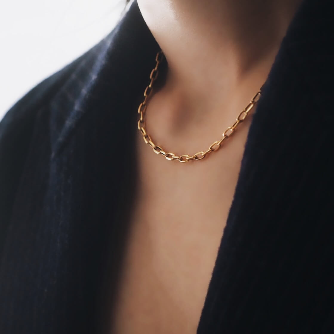 A woman elegantly showcases a gold chain necklace, adding a touch of glamour to her outfit.