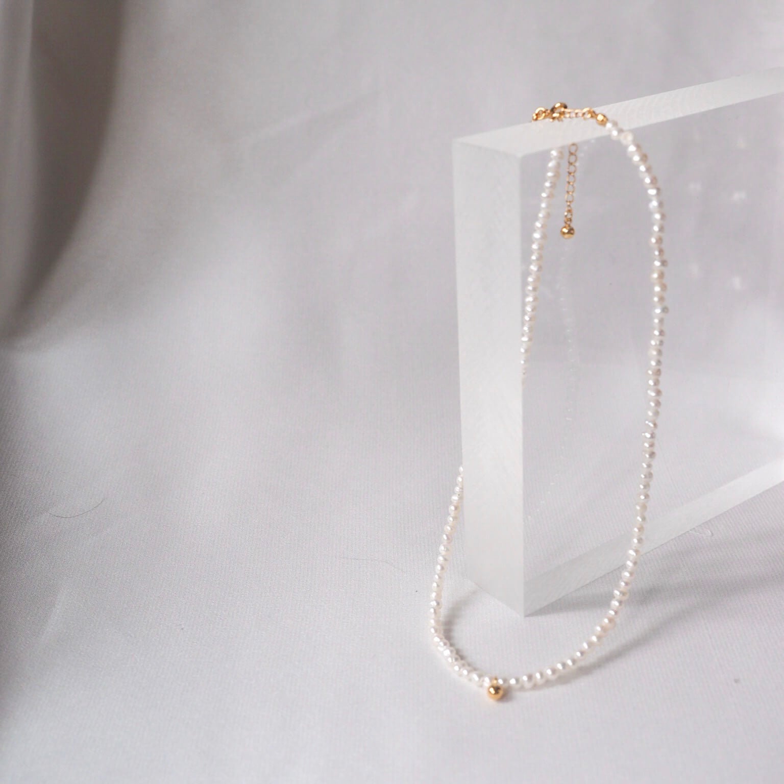 Simple white pearl necklace featuring a gold chain and a tiny golden bean charm, ideal for a subtle, elegant look.