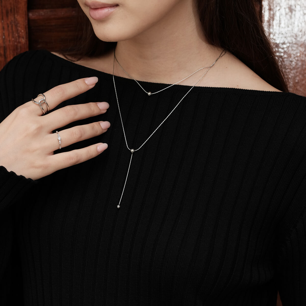 A woman wearing a black sweater models a chic double-layer necklace featuring a ball pendant, perfect for a glamorous touch.