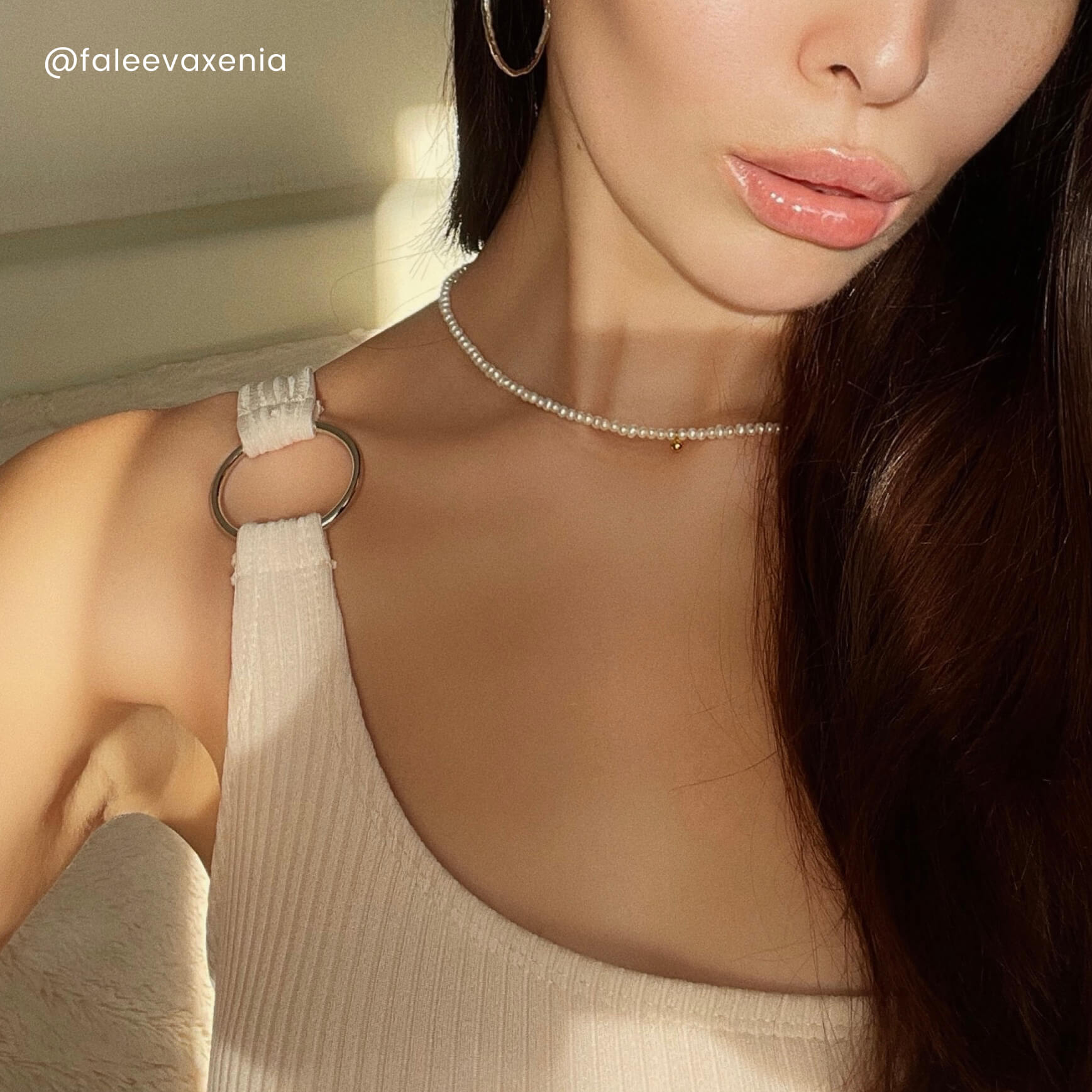 A woman with long brown hair wears a white tank top, showcasing the elegant Tate Pearls Necklace with a golden bean charm.