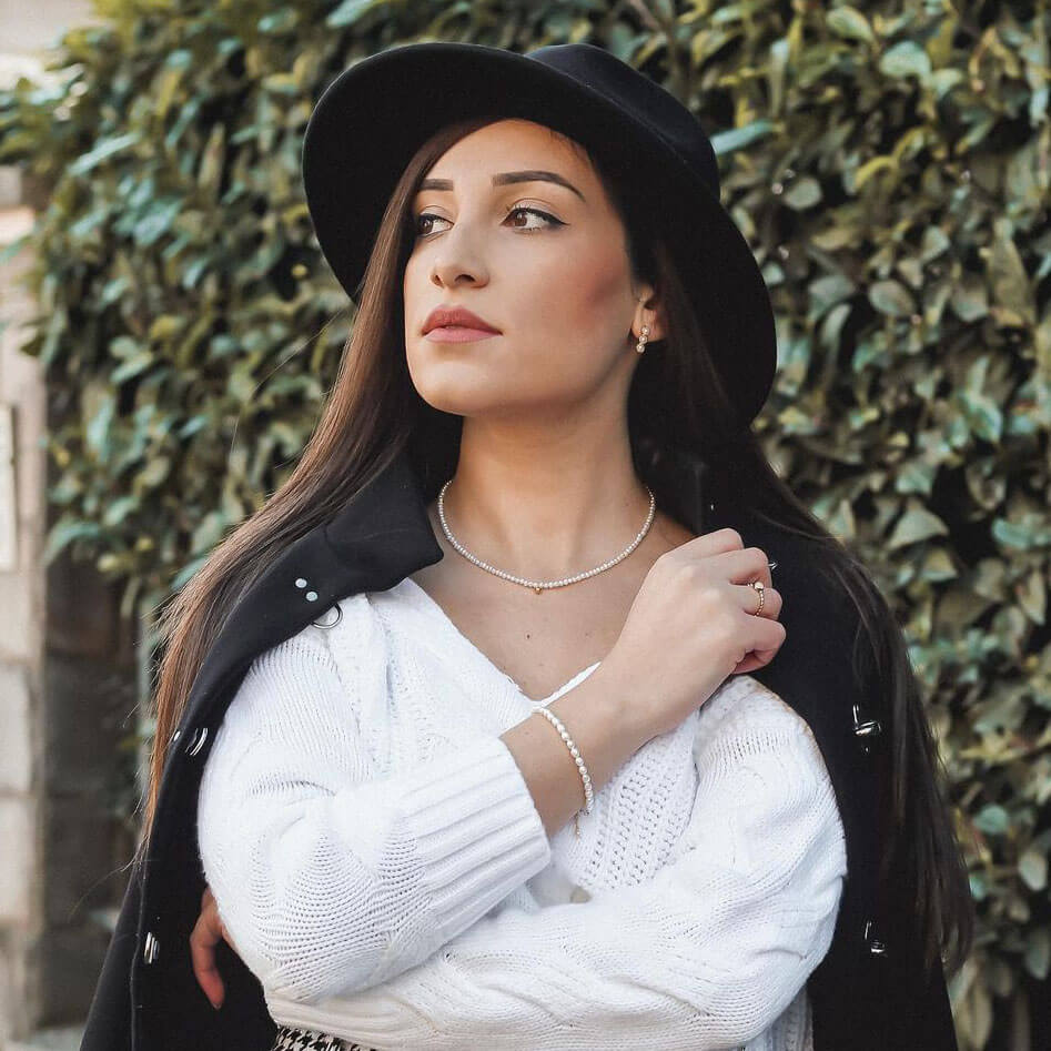 A woman wearing a hat and sweater, highlighting her style with a delicate Tate Pearls Necklace and its charming golden bean.