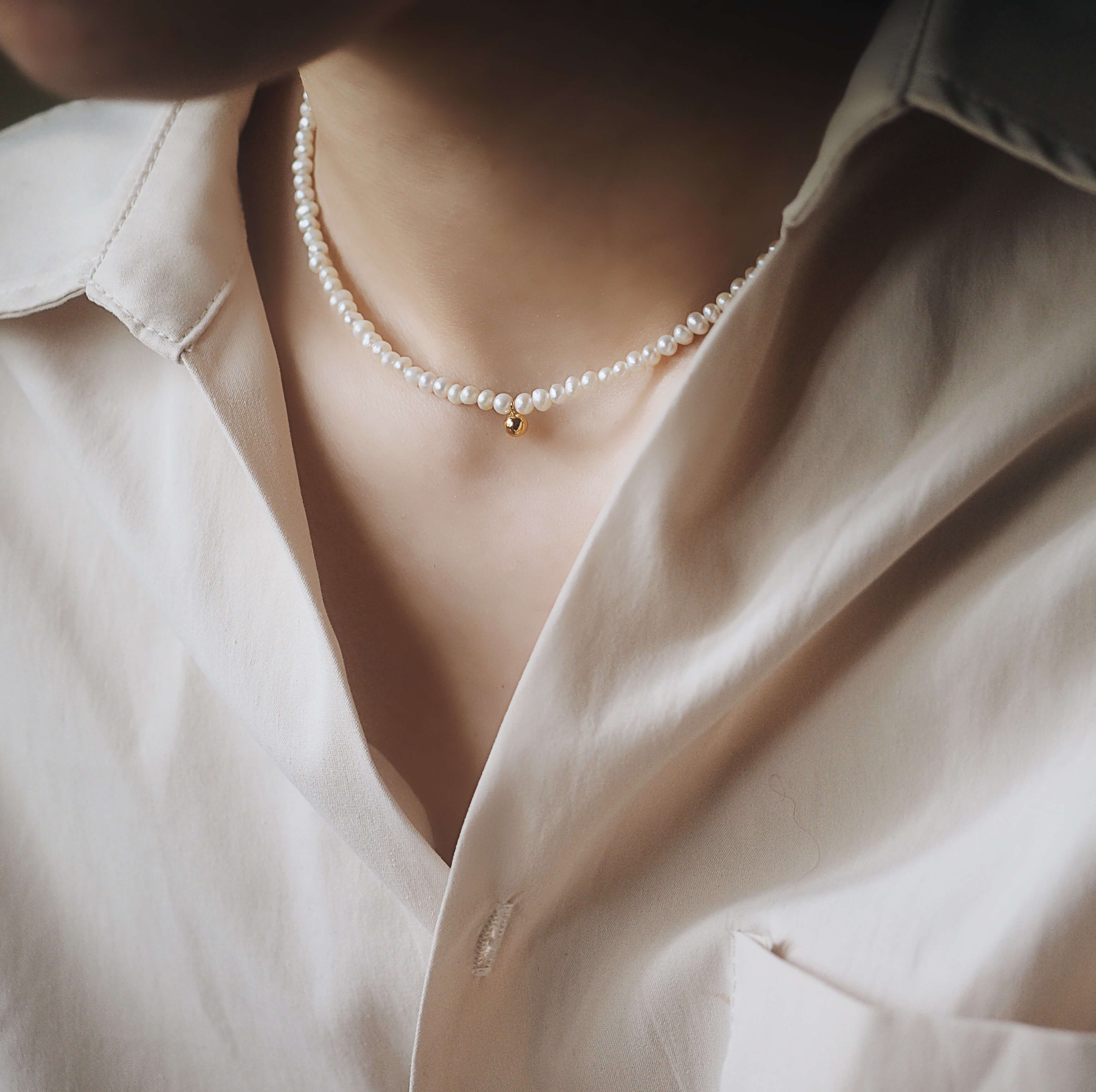 A woman in a white shirt wears a delicate pearl necklace, showcasing a simple and elegant style.