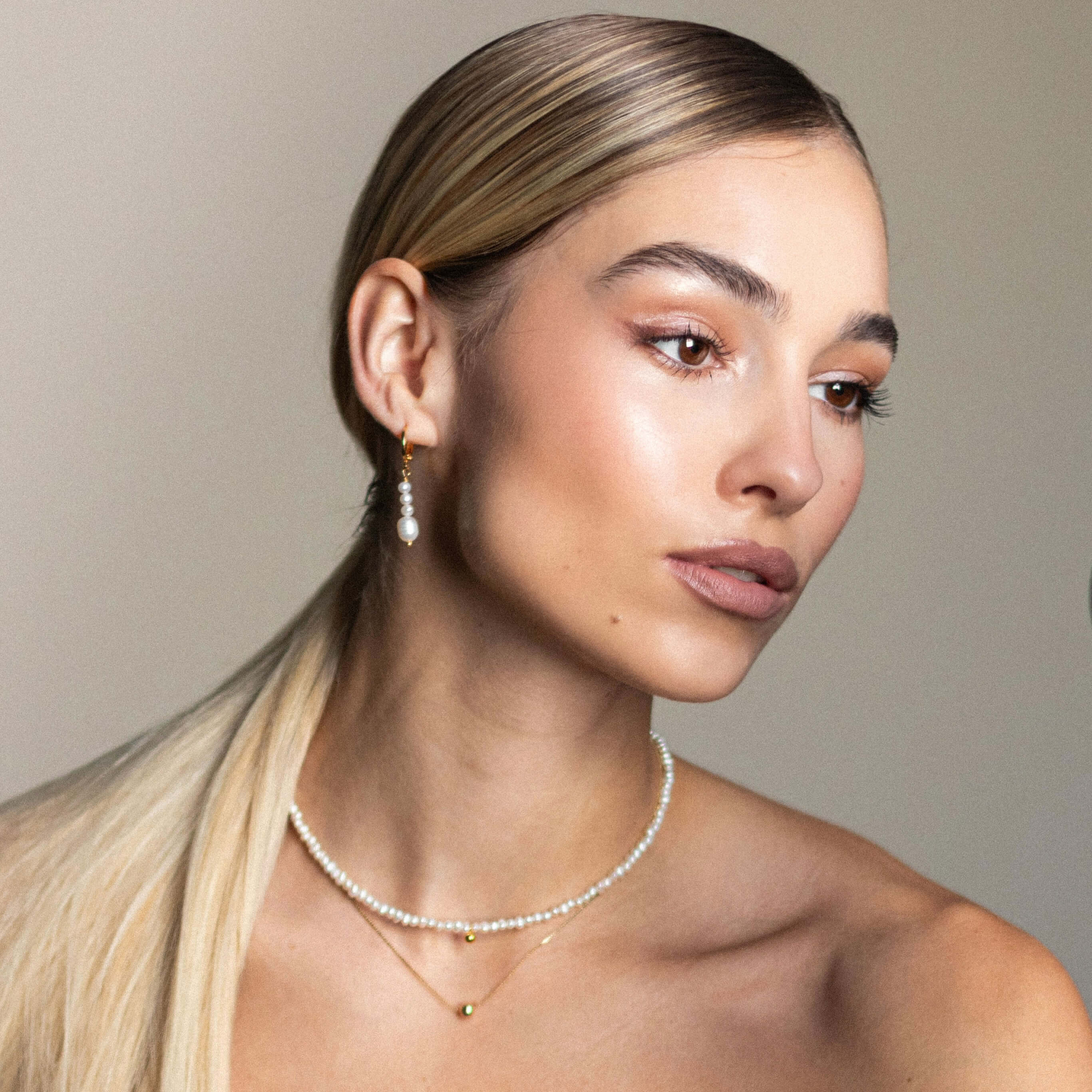 A woman with long blonde hair displays a subtle necklace with a mini golden bean charm, embodying sweet and simple elegance.