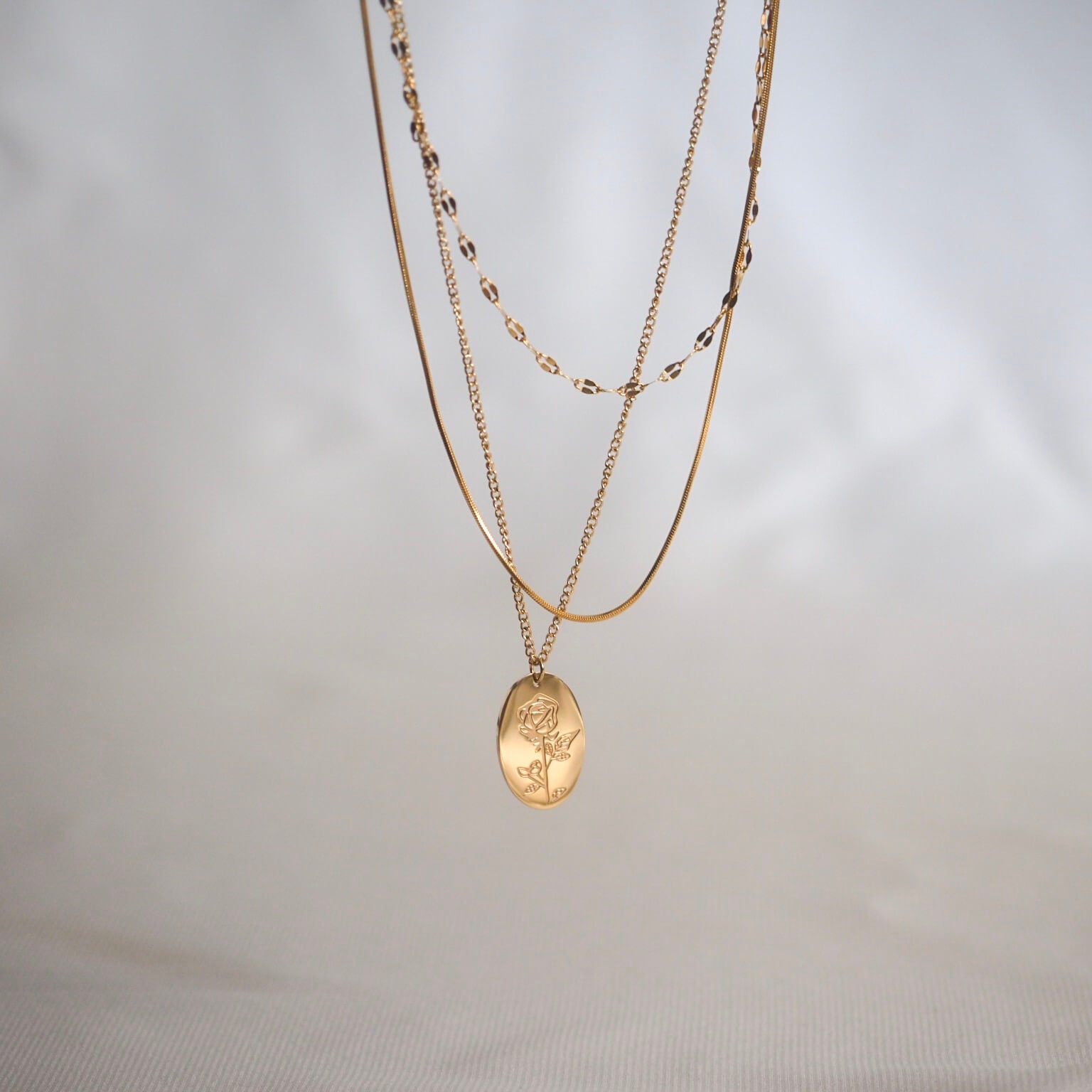 A gold necklace featuring a shiny coin pendant, elegantly displayed against a simple background.