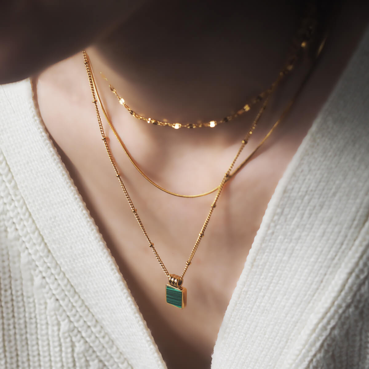 A woman elegantly showcases a gold necklace adorned with vibrant malachite stones, highlighting her sophisticated style.