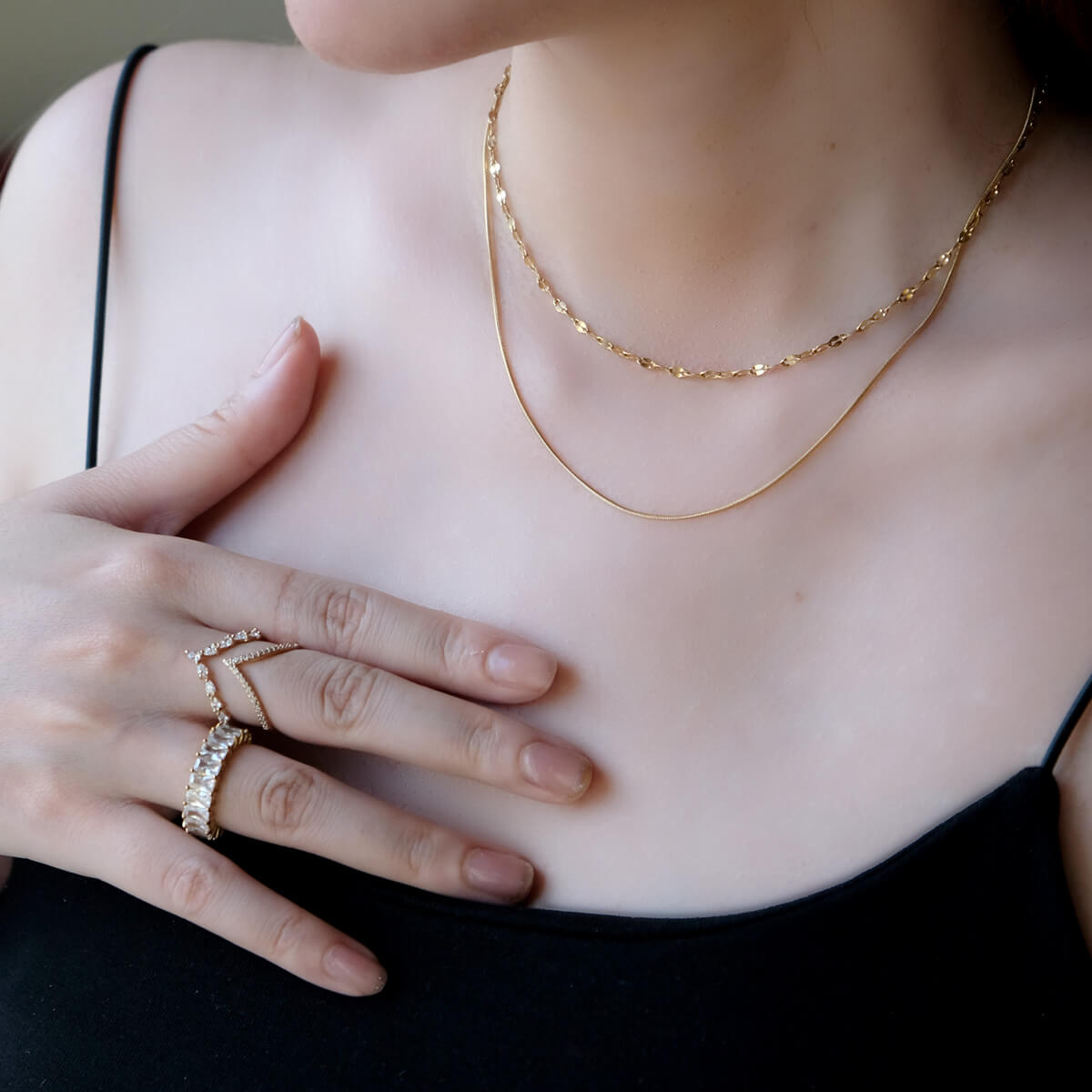 A woman displaying a gold necklace and two rings, highlighting her elegant accessories and fashionable appearance.